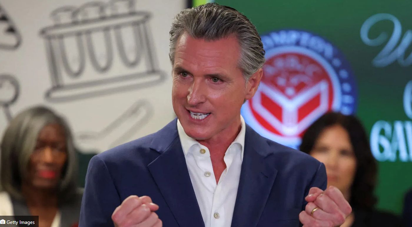 governor Gavin Newsom gestures emphatically during a campaign event with 'W' and 'GAM'