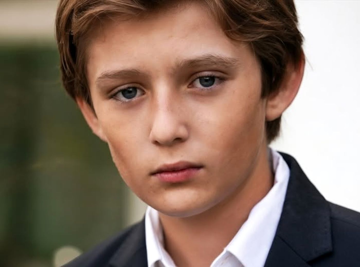 young boy with blue eyes and brown hair wearing a dark suit and white shirt