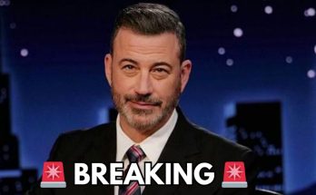 jimmy Kimmel in dark suit with striped tie a nighttime city skyline backdrop